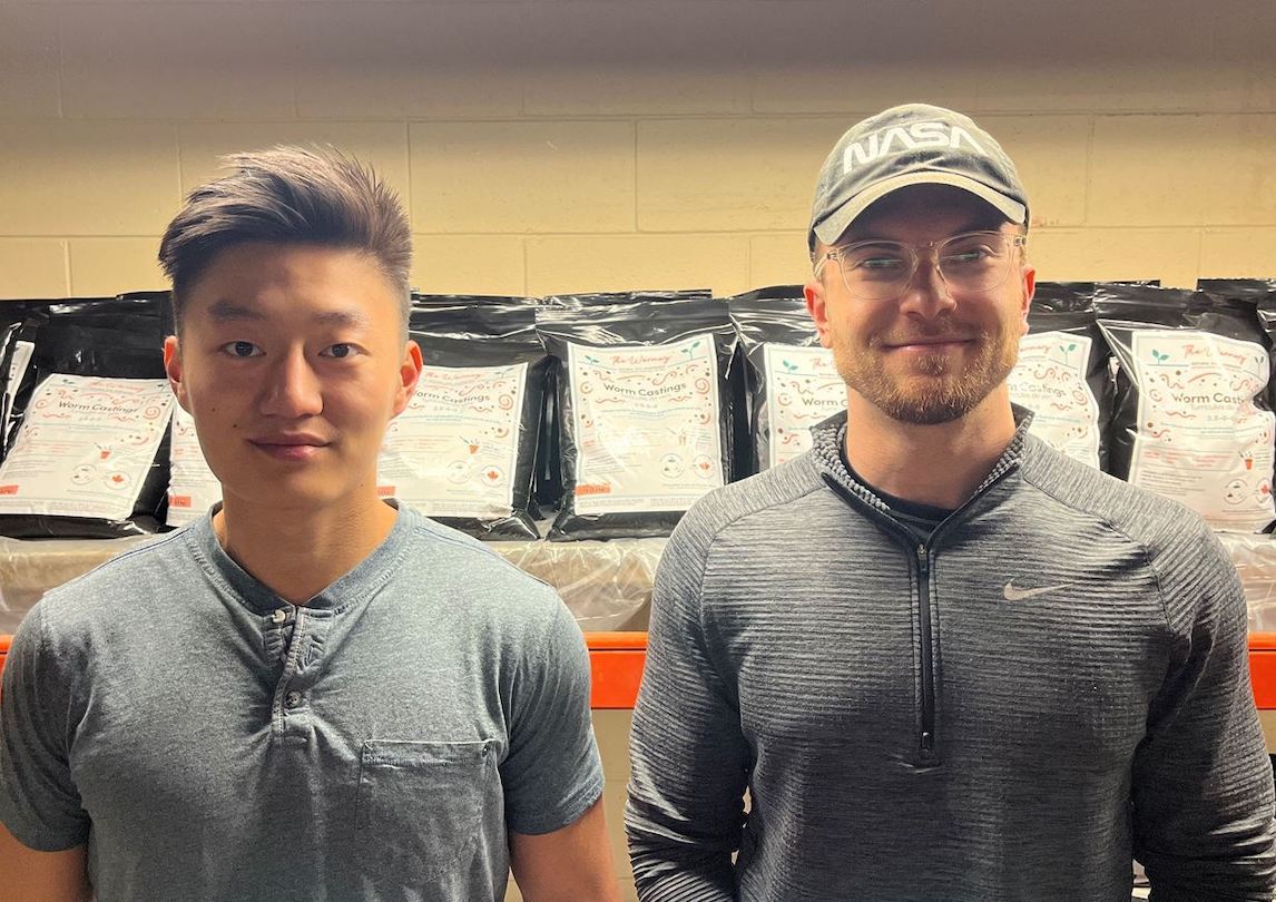 Two Ivey alumni standing in front of packages from their start-up