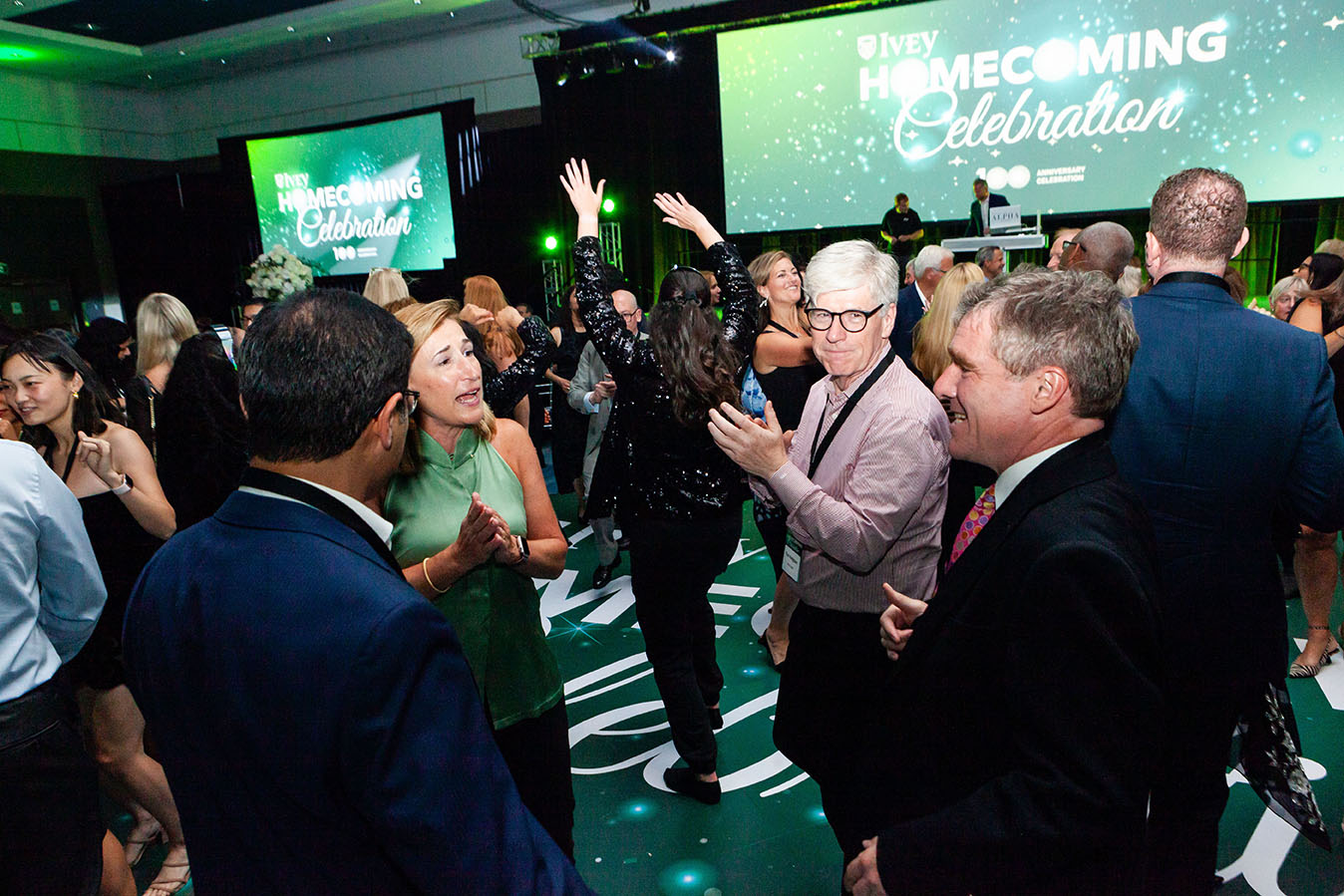 A group of people celebrating at a party. A sign in the background reads: Ivey Homecoming Celebration