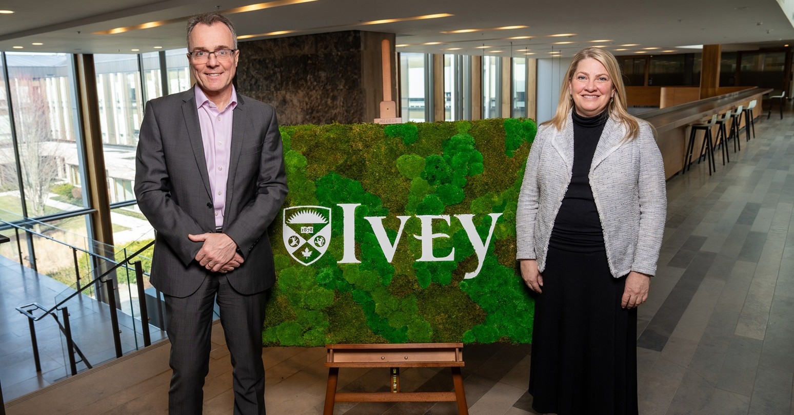 Julian Birkinshaw and Stephanie Brooks standing beside an Ivey sign with a greenery background